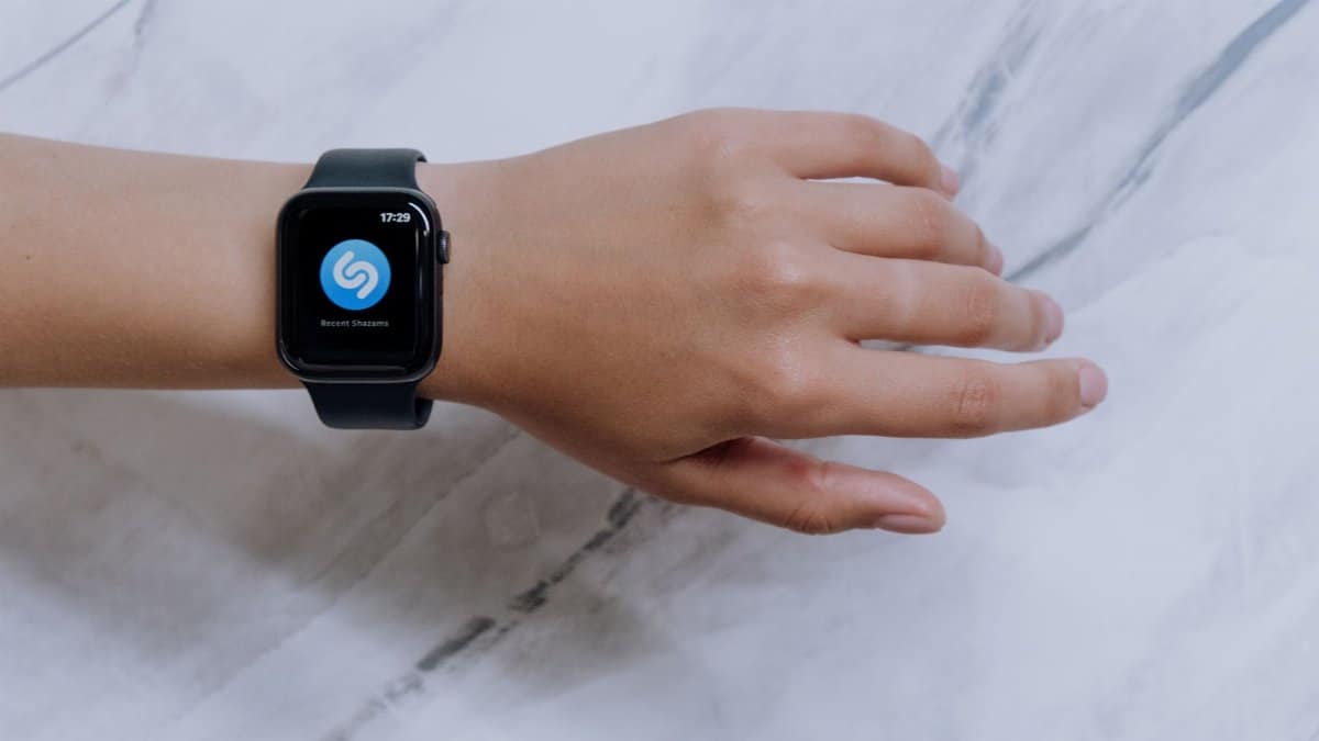 Close-up of a smartwatch on a wrist showing a music identification app with a marble background.