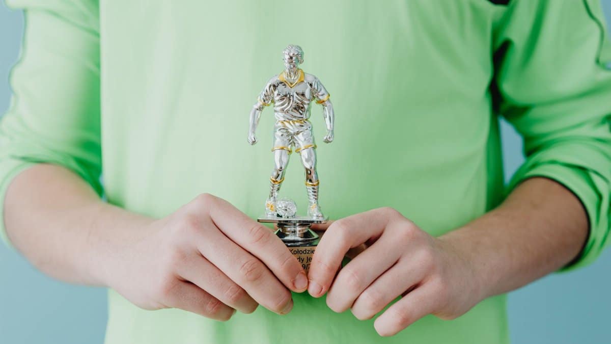 A person holding a silver soccer trophy against a blue background.