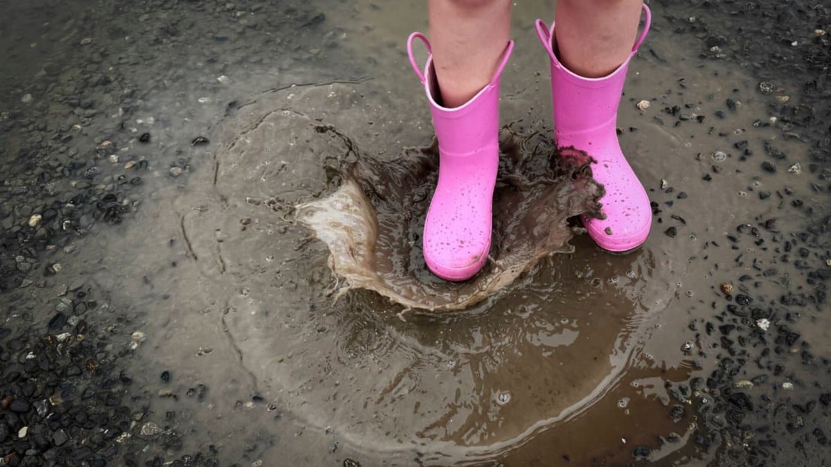 A child jumping in a muddy puddle with bright pink boots during a rainy day in Seattle.