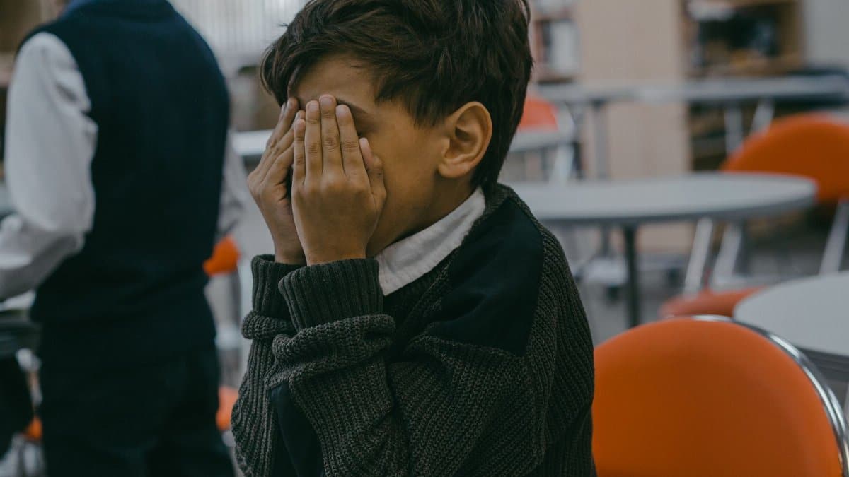 A child with hands covering face, experiencing bullying in a school setting.