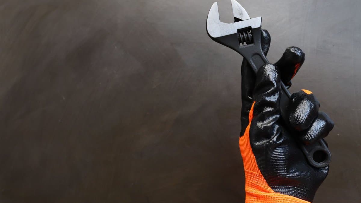 A gloved hand holding an adjustable wrench on a dark background.