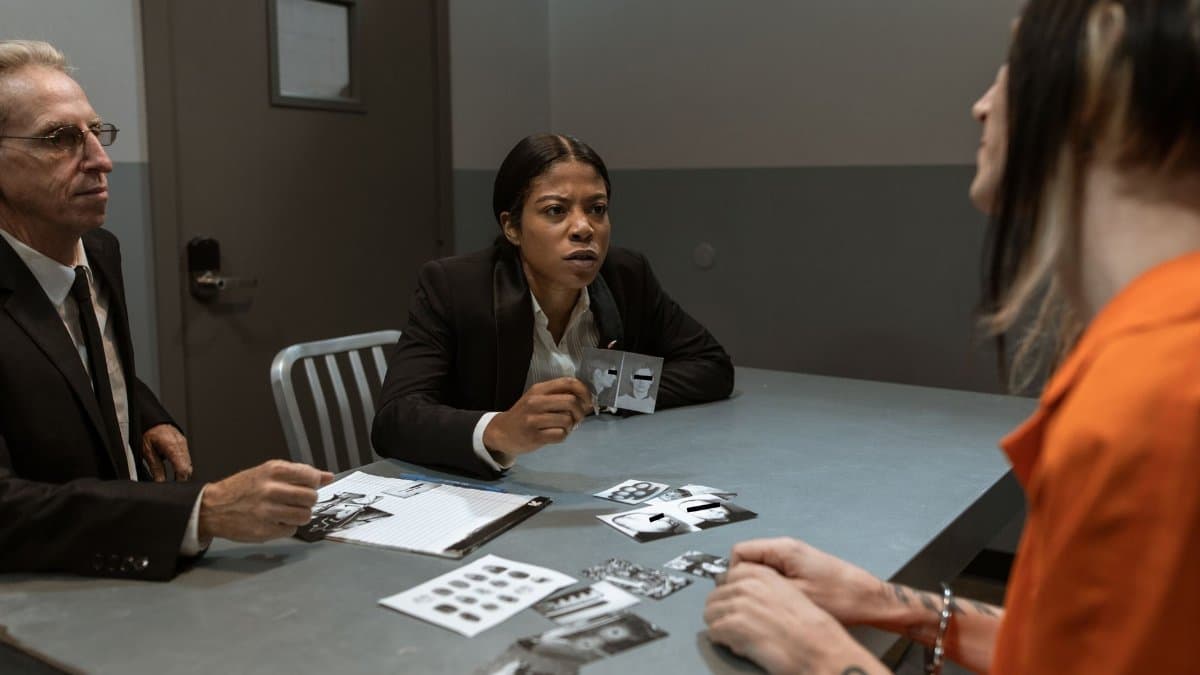 Interrogation scene with detectives questioning a handcuffed suspect inside a jail room.