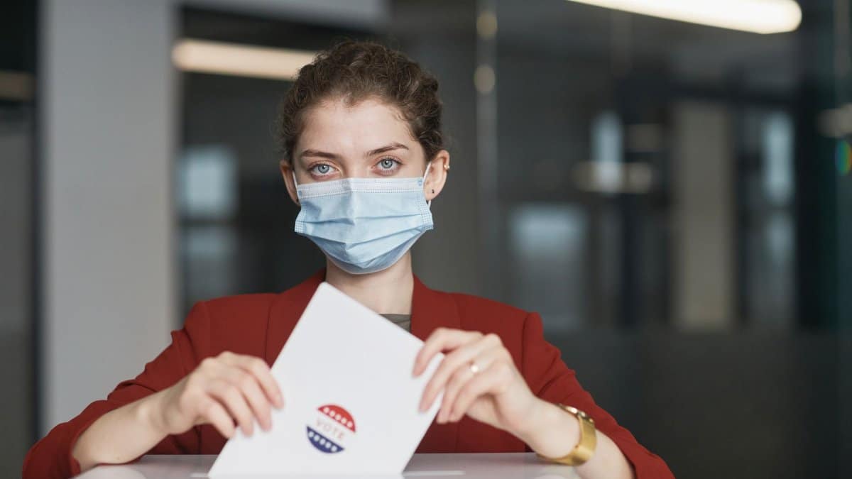 A woman wearing a face mask places a ballot in the box on election day with safety measures.