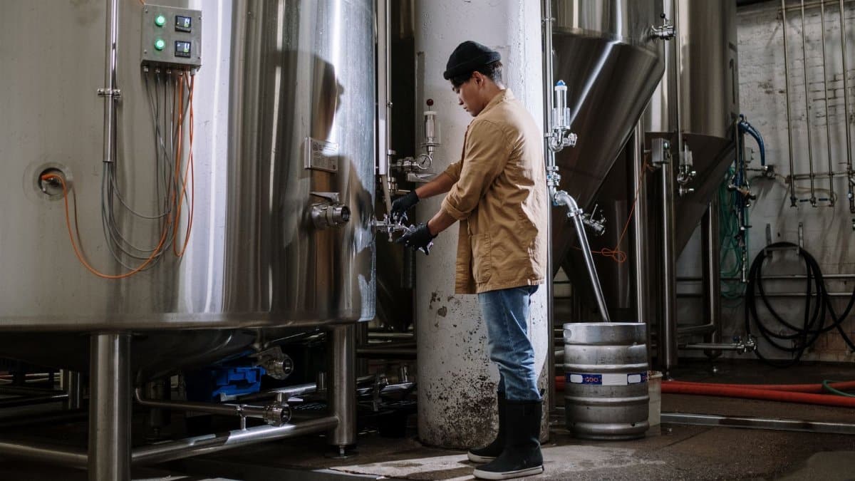 Asian brewmaster working with large stainless steel fermentation tanks in a brewery.