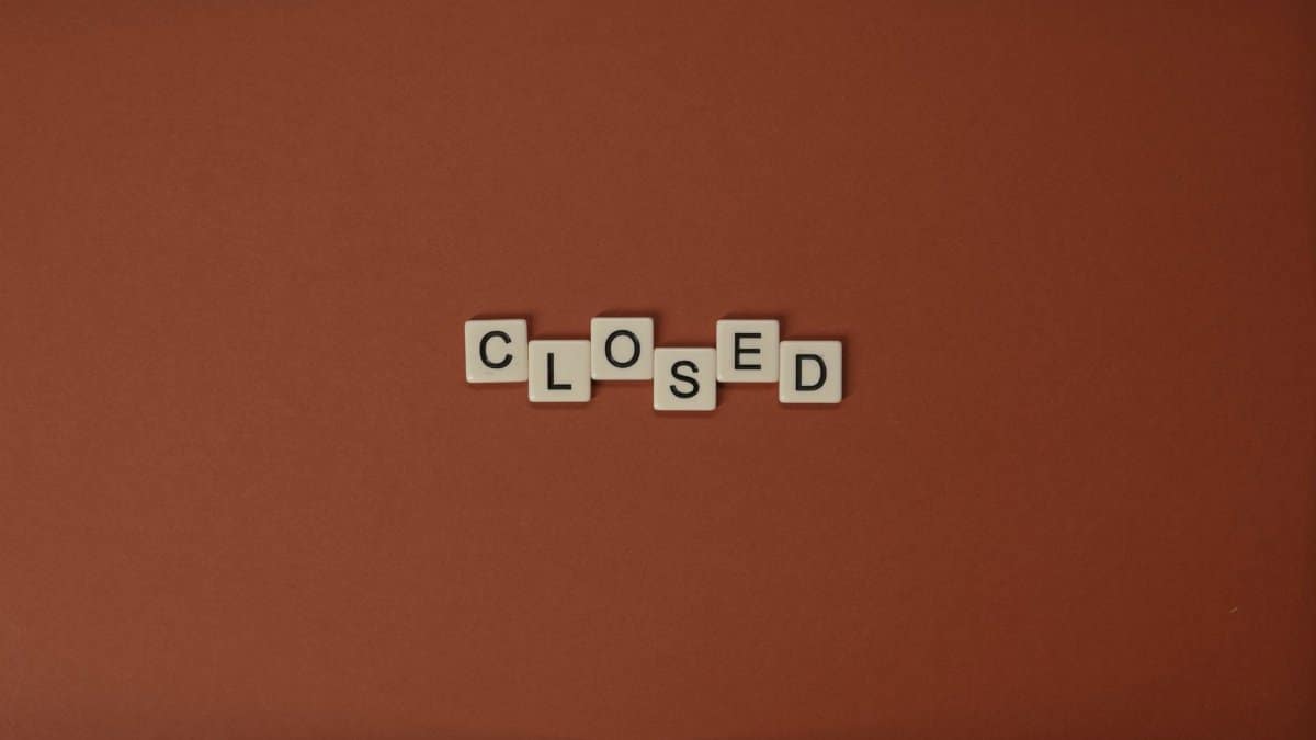 Scrabble letter tiles spelling 'CLOSED' on a brown background, minimalist design.