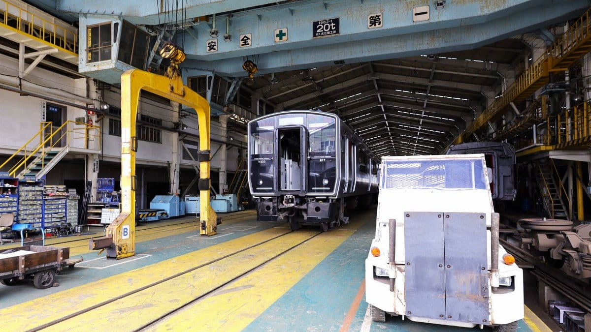 Interior view of a train maintenance facility in Kitakyushu, Japan showing trains and equipment.