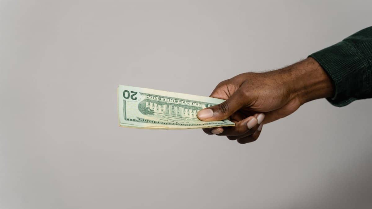 A hand holding a twenty dollar bill against a plain gray background.