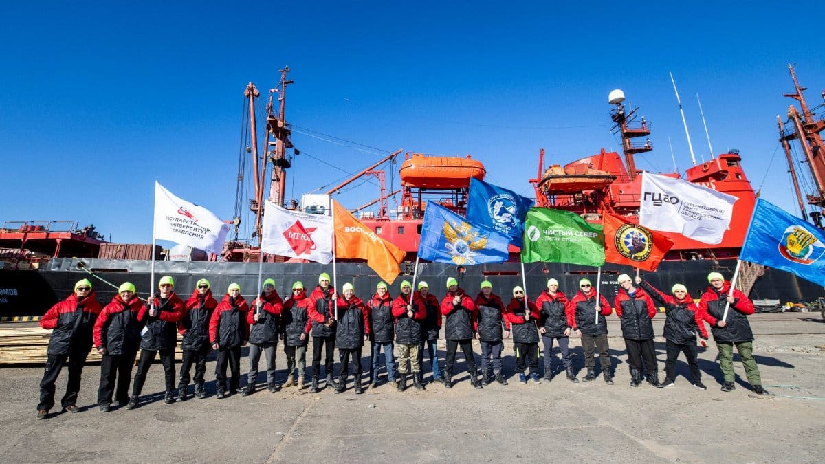 A group of explorers with flags in front of an icebreaker on a sunny day.