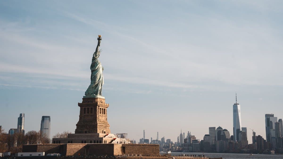 View of the Statue of Liberty with New York City skyline in the background under a clear sky.