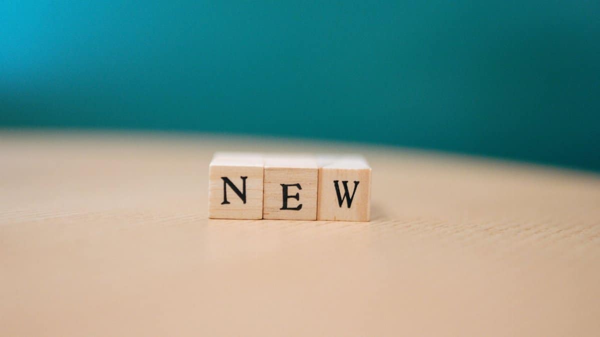 Wooden blocks spelling out 'NEW' on a wooden surface against a teal background.