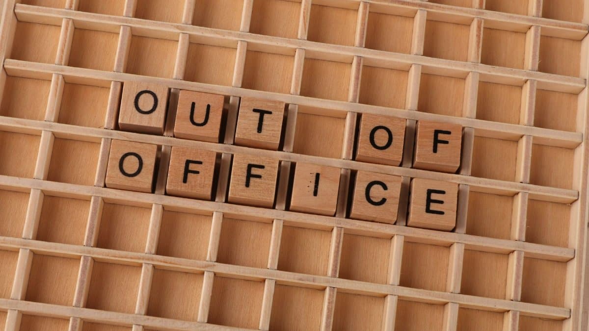 Wooden letter blocks spelling out 'Out of Office' on a wooden grid background.