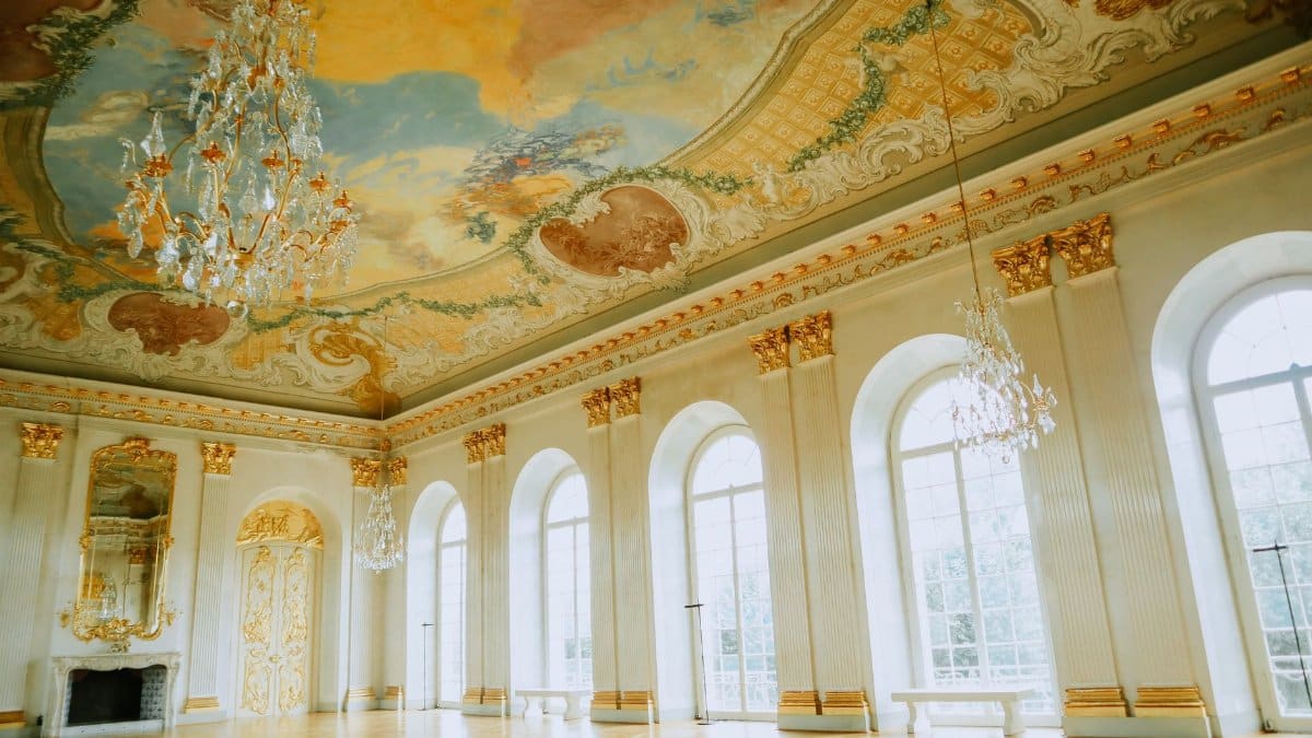 Elegant ballroom featuring a grand chandelier and intricately painted ceiling, exemplifying opulent interior design.
