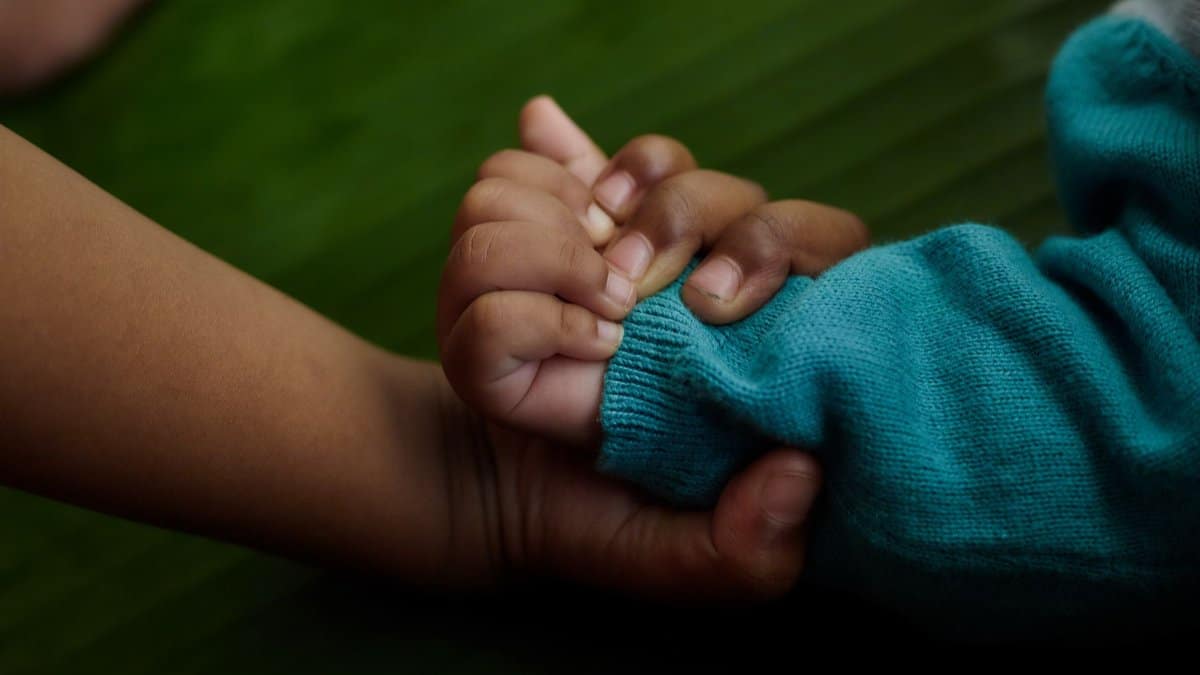 Close-up of a baby's hand holding an adult's for warmth and affection on a green background.