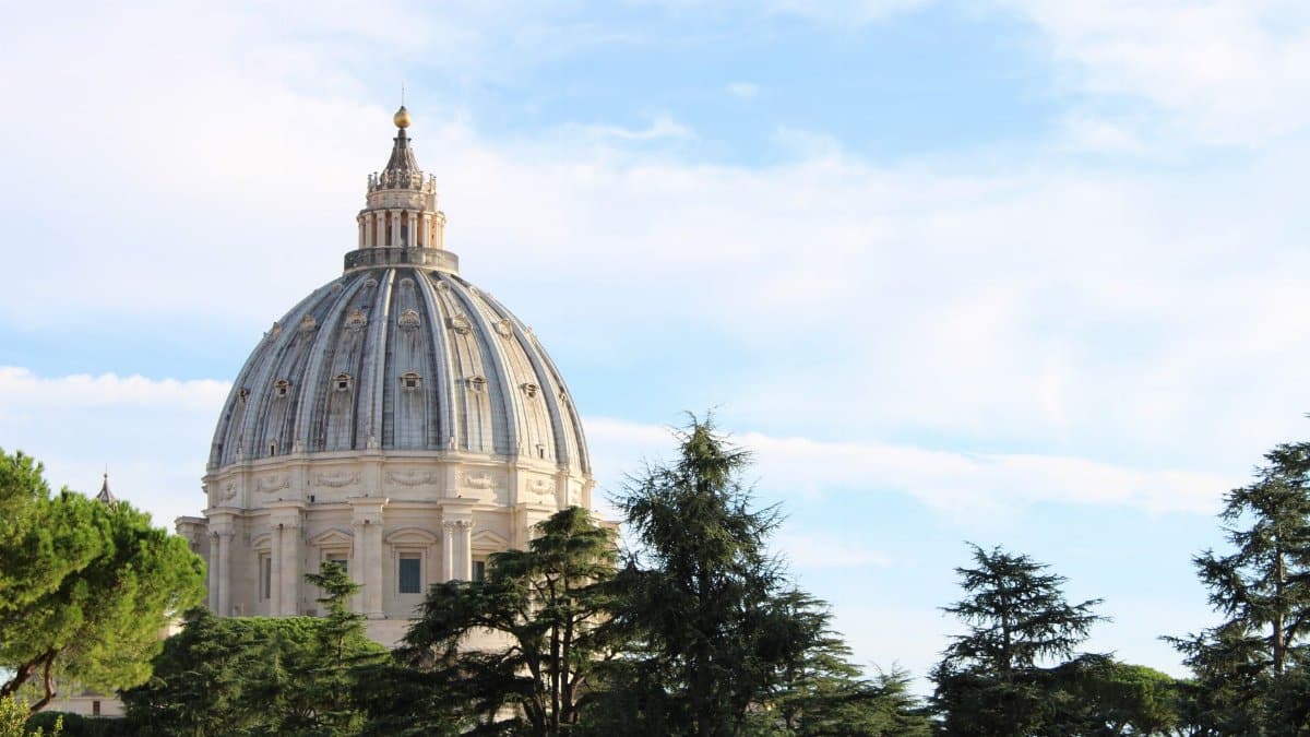 Stunning view of St. Peter's Basilica dome rising above lush greenery in Vatican City.