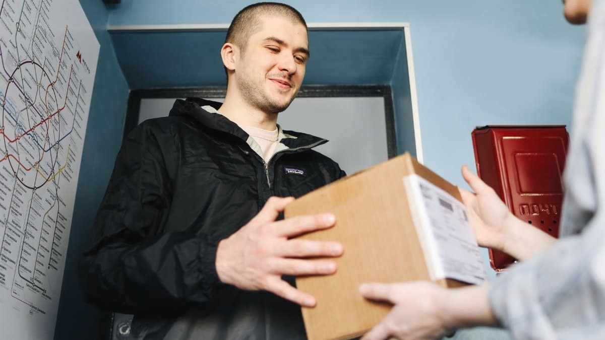 Smiling man receives a package at home apartment entrance.
