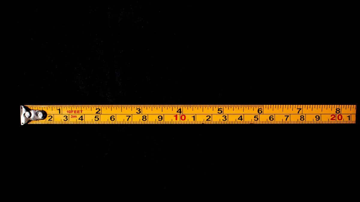 A close-up of a yellow tape measure laid out on a black background.