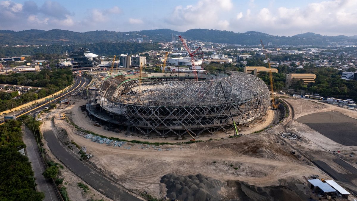 Aerial view of a stadium under construction, surrounded by urban cityscape and hills.