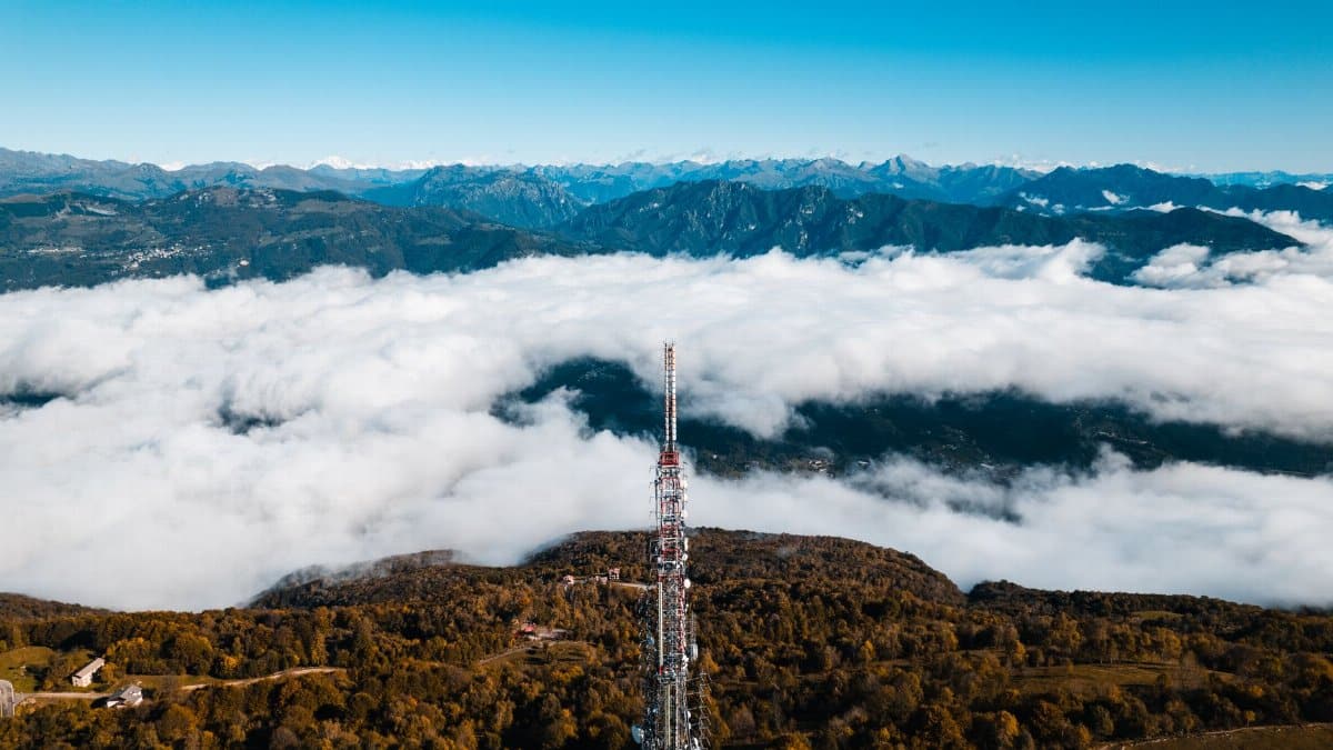 Aerial view of a communications tower surrounded by lush mountains and clouds, offering a dramatic landscape.