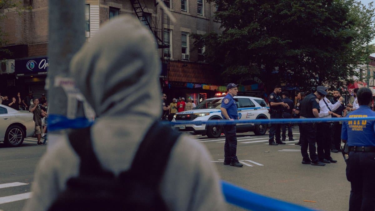 Police officers at an urban scene with a crowd and a cordoned-off area, capturing a street incident.