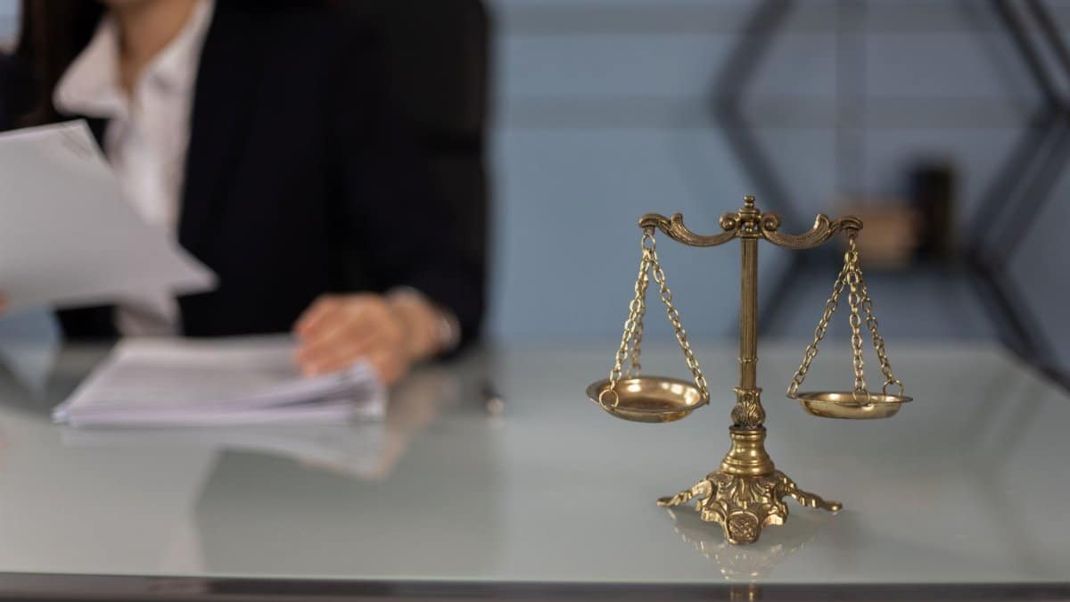 Balance scales on a desk in a professional office with a blurred businesswoman in the background.