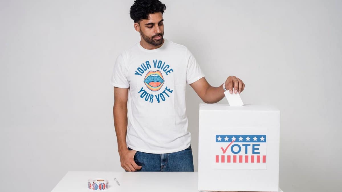 Young man casting a vote into a ballot box on a white background promoting democracy.