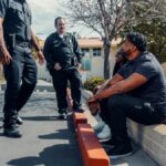 Police officers interacting with individuals seated outdoors in a parking area.