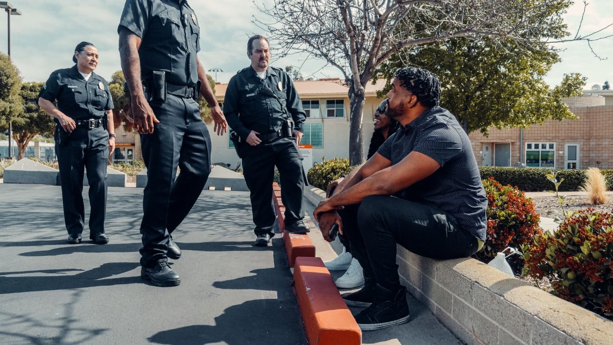 Police officers interacting with individuals seated outdoors in a parking area.