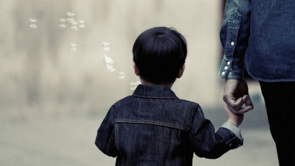 A child and adult walking together holding hands, evoking family bond and care.