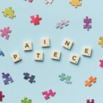 Scattered jigsaw puzzle pieces and Scrabble letters spelling 'PATIECE' on a light blue background.