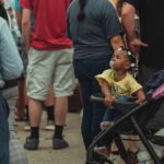 A diverse crowd in a vibrant urban setting featuring a child in a stroller.