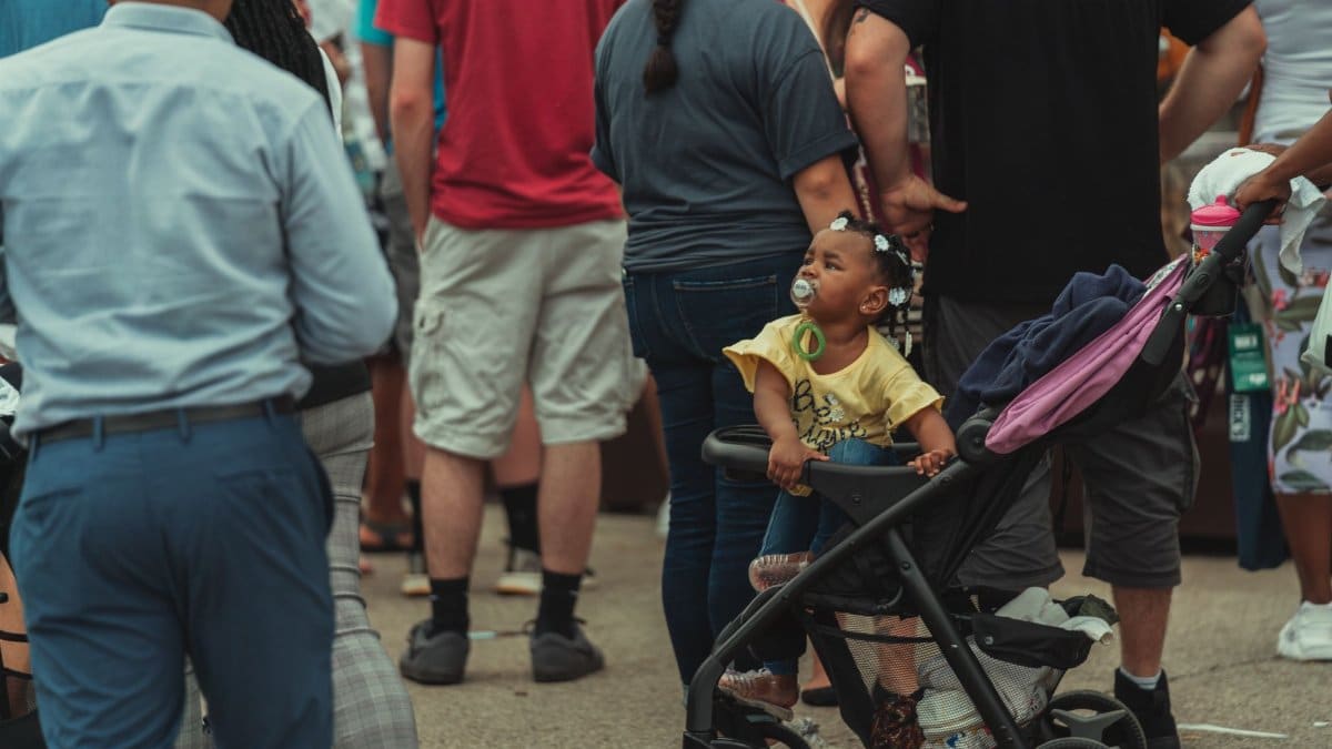 A diverse crowd in a vibrant urban setting featuring a child in a stroller.