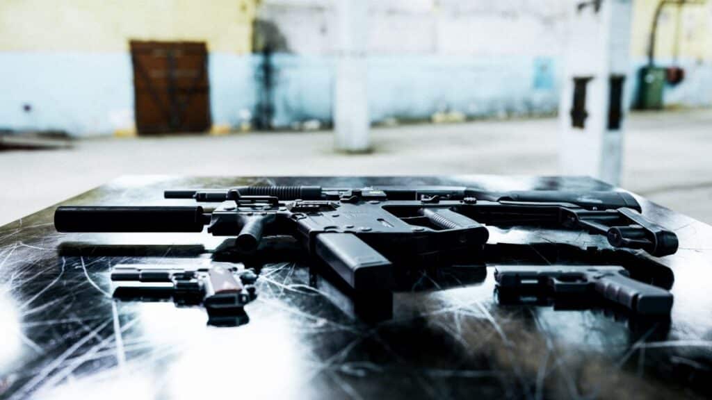 Various firearms displayed on a scratched metal table in an industrial setting.