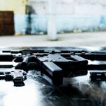 Various firearms displayed on a scratched metal table in an industrial setting.