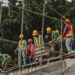 Construction workers in safety gear work on a structure outdoors, emphasizing teamwork and safety.