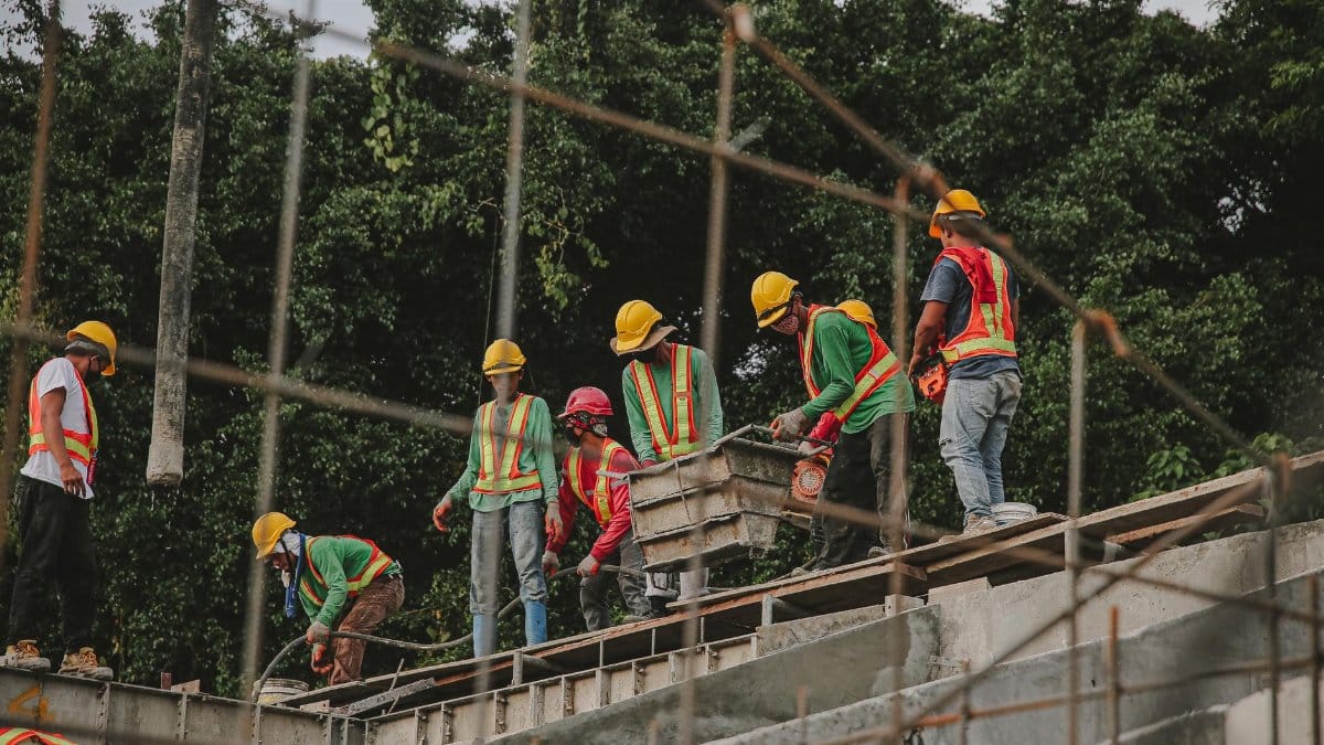 Construction workers in safety gear work on a structure outdoors, emphasizing teamwork and safety.
