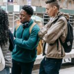 Multiethnic classmates in casual outfits and backpacks standing on city street near buildings and benches while having argument