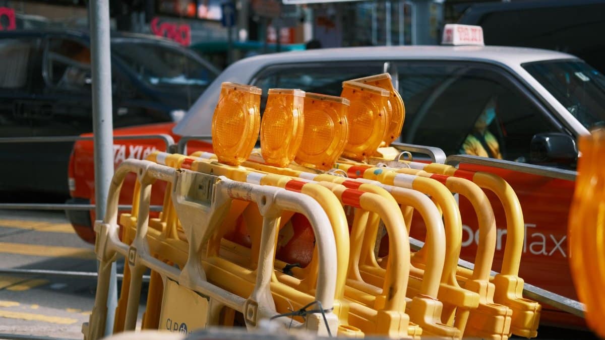 Traffic barriers with yellow lights in a city street with taxis in the background.
