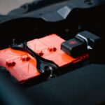 Detailed view of an orange car battery inside a vehicle's engine bay, highlighting its features.