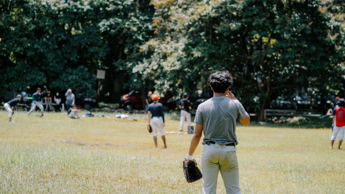 Group of athletes playing baseball in a sunny park with trees in the background.