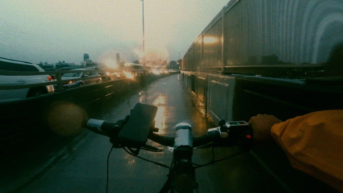 Cyclist navigating a wet bike lane in rainy New York City with blurred traffic lights.