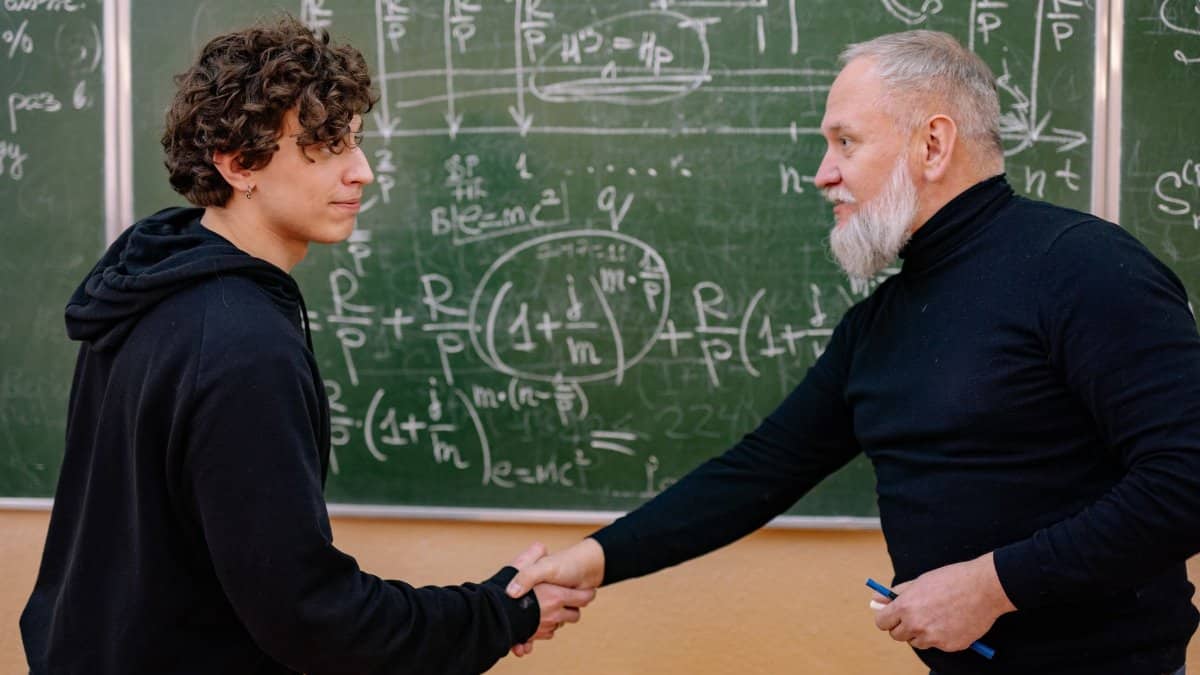 A professor and student shake hands in front of a chalkboard filled with mathematical formulas, symbolizing education and mentorship.