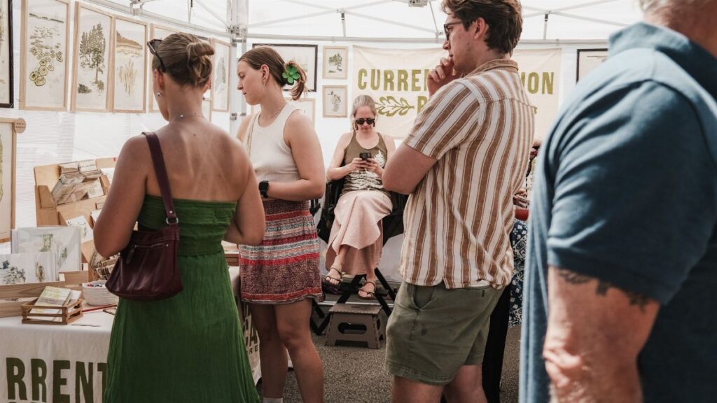 People browsing artwork at an outdoor market in Chicago, IL under a tent.