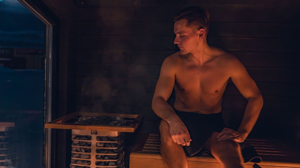 A shirtless man relaxes in a modern Nordic sauna, experiencing the warmth and benefits of steam.