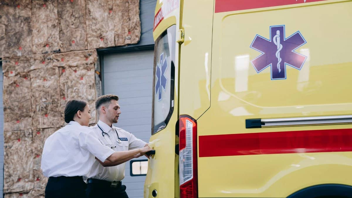 Two paramedics close the rear doors of an ambulance, preparing for emergency response.