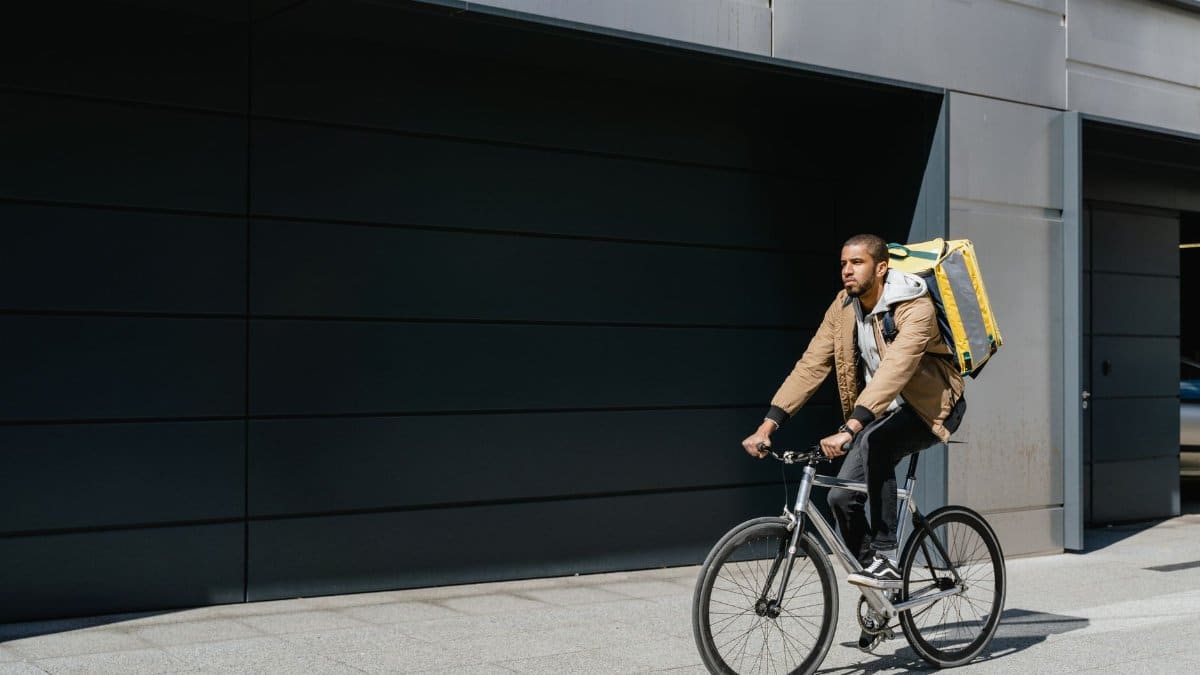Delivery cyclist with backpack rides through city street, showcasing modern urban logistics.