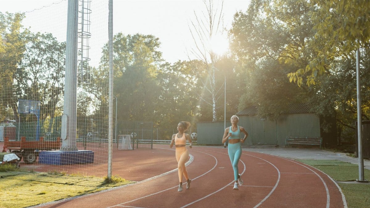Two women jogging on an outdoor track, enjoying exercise and fitness in the morning sun.