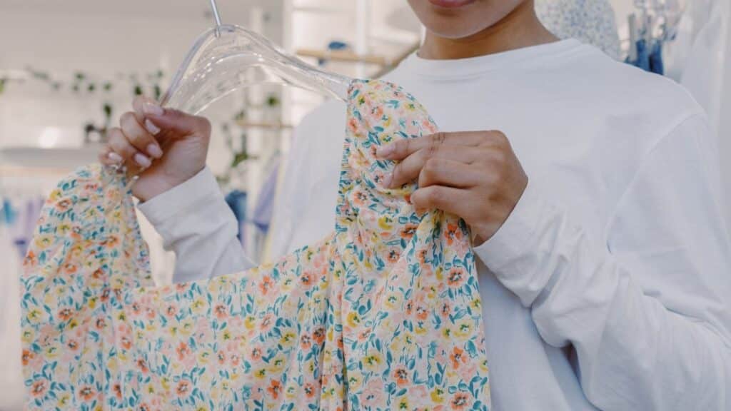 Close-up of a woman holding a floral dress on a hanger inside a boutique store.