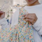 Close-up of a woman holding a floral dress on a hanger inside a boutique store.
