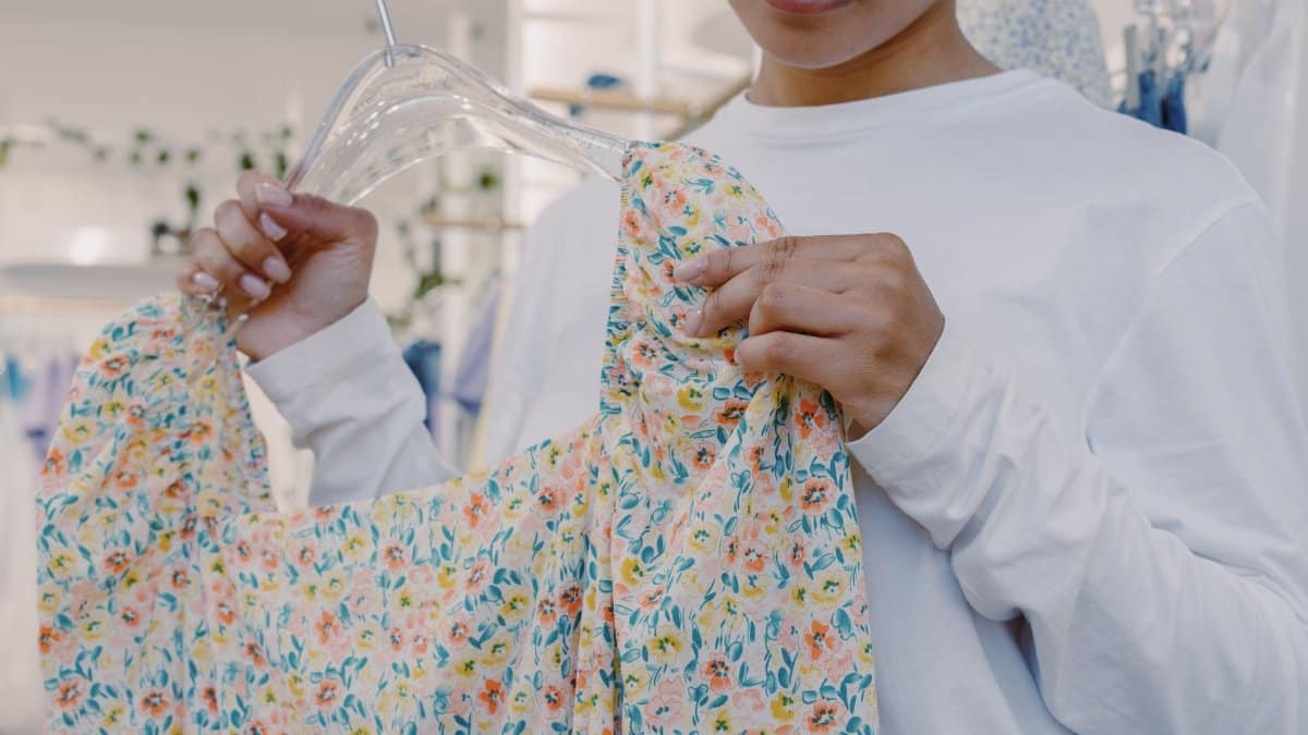 Close-up of a woman holding a floral dress on a hanger inside a boutique store.