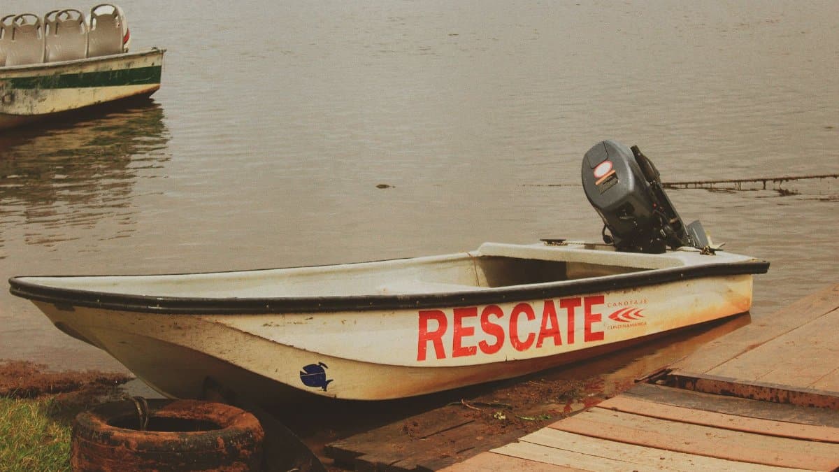 A rescue boat titled 'RESCATE' docked by a calm lakeside, ready for emergency use.